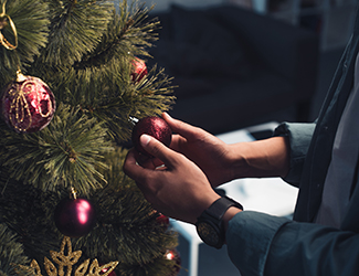 Hands placing an ornament on a Christmas tree