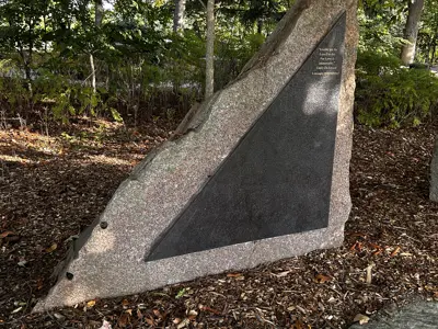 large triangular stone in forest with triangular metal sign on it